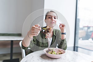 girl sits in a restaurant near the window and directs a fork with a salad to the camera photo