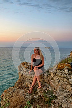 Girl sits on a rock and looks at a beautiful view of the sea and sunset