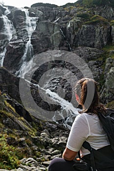 The girl sits on a rock and looks towards the waterfall Wielka Siklawa