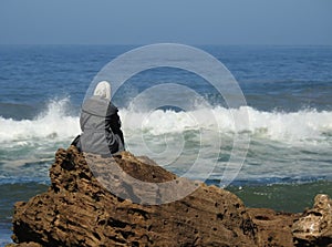 A girl sits on the rock watching the waves
