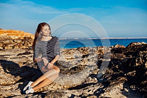 Girl sits on the rocky beach enjoys sunshine