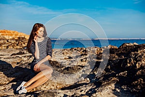 Girl sits on the rocky beach enjoys sunshine