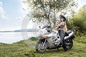 Girl sits on  sports bike on the background of lake