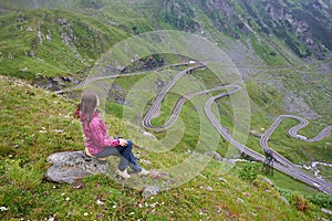 Girl sits on stone enjoying wonderful mountain scenery. Transfagarashan Highway