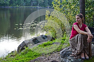 The girl sits on stone in the forest, by the lake. Quiet romantic photo