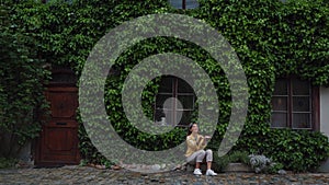 Girl sits on a stone near House covered growing plants in fabulous city Krumlov