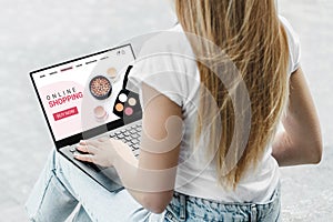 A girl sits on the street looking at a laptop screen and orders cosmetics on the website