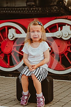 A girl sits on a suitcase on the platform at the station near the train. Bitter tears. To be late for the train, not to leave.