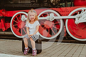 A girl sits on a suitcase on the platform at the station near the train. Bitter tears. To be late for the train, not to leave.