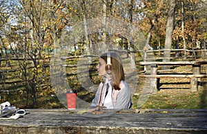a girl sits at a table in an autumn park, headphones are on her head