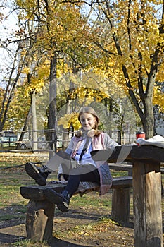 a girl sits at a table in an autumn park, headphones are on her head