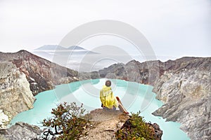 The girl sits on top of the volcano and looks at the lake in the crater