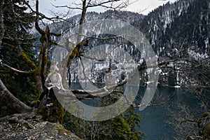 Girl sits on a tree and meditates near lake Ritsa in Abkhazia