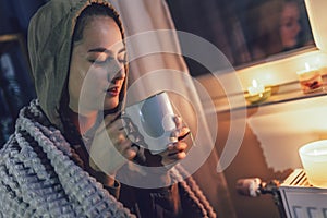 Girl sits under blanket near heating radiator with cup of tea.Rising costs in private households for gas bill due to