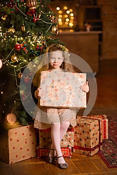 girl sits under the Christmas tree, and holds a New Year& x27;s gift box in her hands