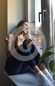 The girl sits on the windowsill and drinks coffee