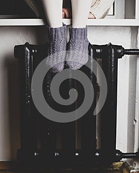 Girl sits on a windowsill put their feet in woolen socks on the radiator and heated on a cold winter evening