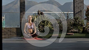 Girl sits in yoga position on terrace against hill