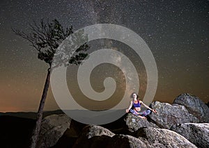 Girl sitting alone with closed eyes on top of huge boulder doing yoga