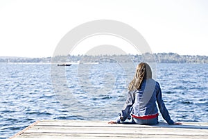 Girl sitting alone on dock by lake