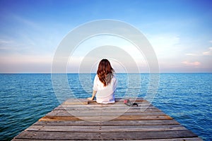 Girl sitting alone on a the wooden bridge on the sea.