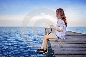 Girl sitting alone on a the wooden bridge on the sea.