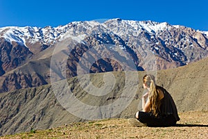 Girl sitting on arid ground looking at Andes snowy mountain range