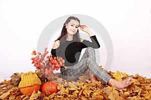 Girl sitting on autumn leaves by pumpkins and flowers