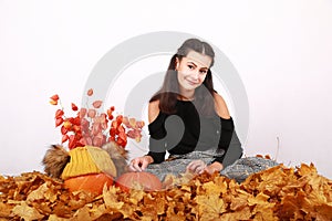 Girl sitting on autumn leaves by pumpkins and flowers