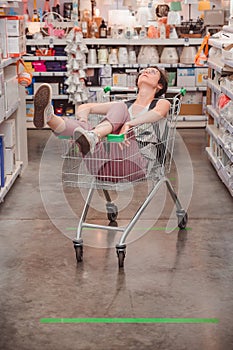 Girl is sitting in a basket in the trading floor. A lady rides in a cart in an empty store