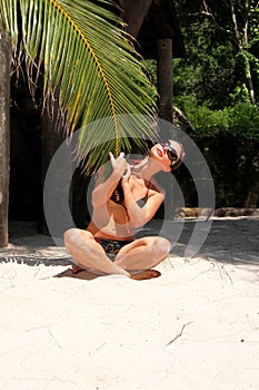 Girl sitting on the beach and holding a palm branch.