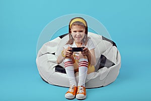 Girl sitting on bean bag chair, holding joystick and playing video game