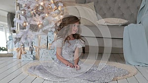 The girl is sitting in a beautiful shiny dress. Christmas interior