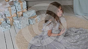 The girl is sitting in a beautiful shiny dress. Christmas interior