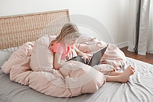 Girl sitting in bed and learning in virtual online school class. Kid typing working on a laptop Internet at home. Child using