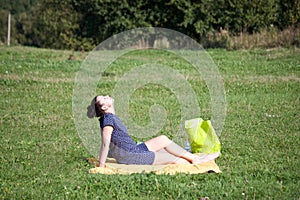 Girl sitting on the bedspread. In a green meadow. Warm autumn days