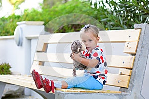 Girl sitting on the bench and cuddling monkey toy