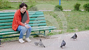 Girl sitting on a bench in the Park city and feeds the pigeons.