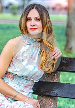 A girl sitting on a bench in the park. Light summer dress, floral print