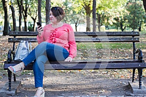 Girl Sitting on the Bench in a Park and Using Cellphone