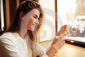 A girl is sitting in a cafe and using a smartphone