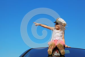 Girl sitting on car roof showing by finger