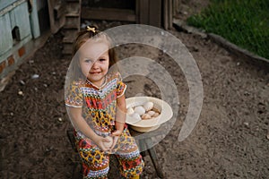 A girl is sitting on a chair near the chicken coop and holding a egg