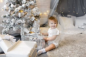 A girl is sitting with a Christmas gift in a silver wrapper of a children`s room