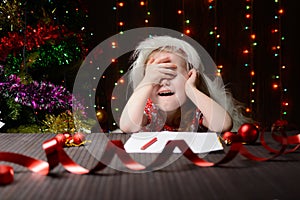 Girl sitting in a Christmas interior, covering eyes with hands