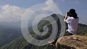 The girl is sitting on the cliff and taking photo