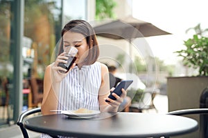 A girl sitting in coffee shop using a phone and smiling