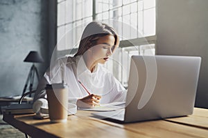 Girl sitting concentrated at laptop and studying remotely. Student using online opprotunities for distant education.