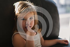 Girl sitting on couch. Girl with enthusiasm and thoughtfully looks slightly to left. one put a finger to his mouth.