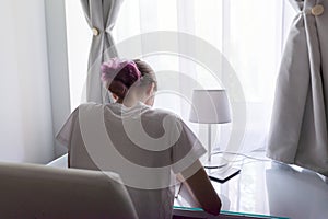 Girl sitting at desk near window, back view, student studying at home